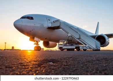 White wide body passenger airplane with a boarding stairs at the airport apron in the evening sun