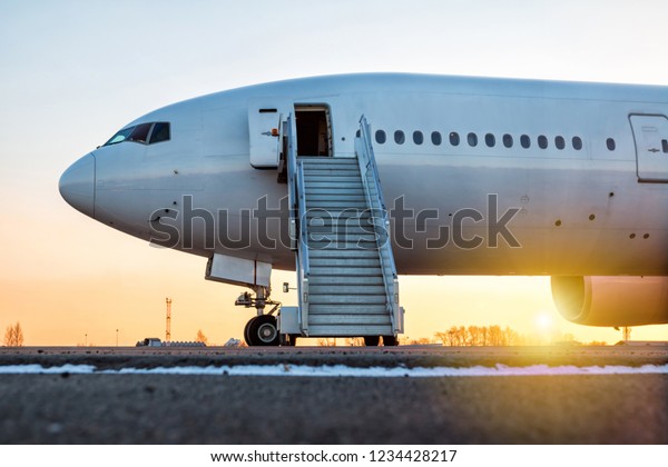 White wide-body passenger\
aircraft with a boarding steps at the airport apron in the evening\
sun