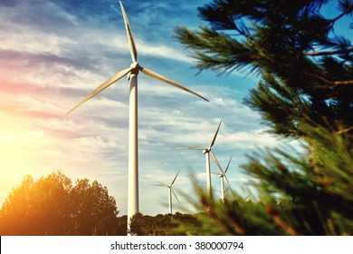 White wind turbine located outside the city, electric generator against beautiful cloudy sky and sunset, alternative energy resources, windmill in field at evening 