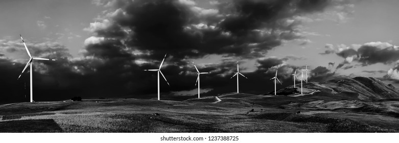 White wind turbines against the backdrop of beautiful mountainous terrain and thunderclouds.