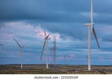 White Wind Turbines Installed In Scandinavian Tundra, Background Blue Sky Sunset.
