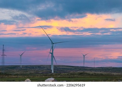 White Wind Turbines Installed In Scandinavian Tundra, Background Blue Sky Sunset.