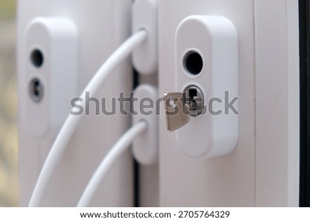 White window handle with key inserted into lock. Security and safety concept for home or office. Modern PVC window frame detail.