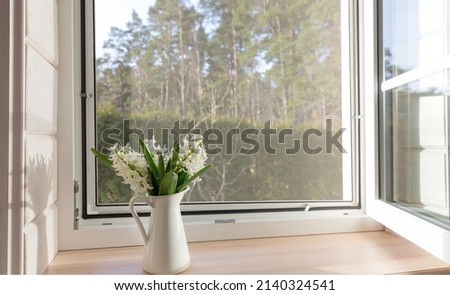 White window with mosuito net in a rustic wooden house overlooking the blossom garden.