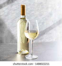 White wine bottle and wine glass on grey concrete background. Wine making and wine degustation concept.