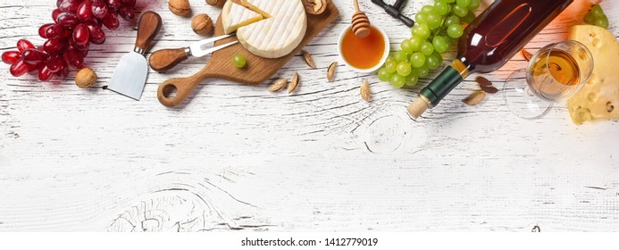 White wine bottle, grape, honey, cheese and wineglass on white wooden board. Panoramic top view with copy space for your text.