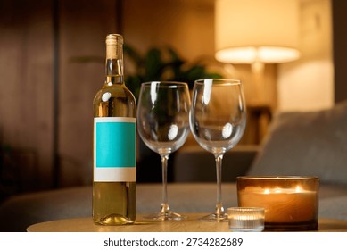 White wine bottle, two empty wine glasses and burning candles on table in cozy interior. Concept of romantic evening, date night and relaxation at home