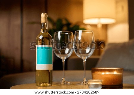 White wine bottle, two empty wine glasses and burning candles on table in cozy interior. Concept of romantic evening, date night and relaxation at home