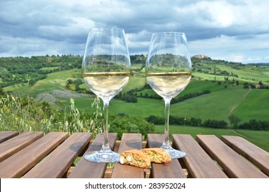 White wine and cantuccini on the wooden table against Tuscan landscape, Italy
