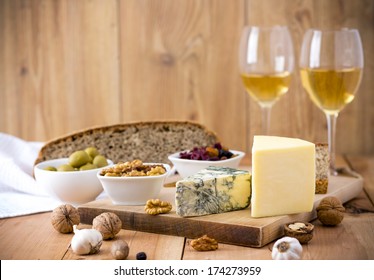 White Wine, Cheese, Nuts, Olives, Dried Fruit, Bread And Garlic On Wooden Table