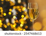 White wine in glass against blurred Christmas lights, space for text. Bokeh effect