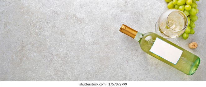 White wine in a glass, bottle, grapes and cork on a gray stone table. Top view. Banner. Copy space of your text.