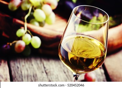 White wine in a glass with fall grapes, old wooden background, selective focus