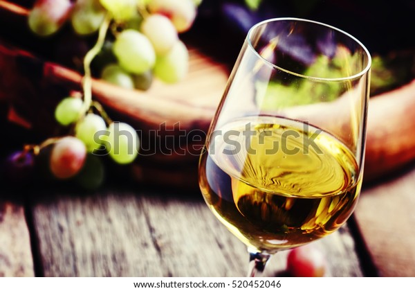White wine in a glass with fall grapes, old wooden\
background, selective\
focus