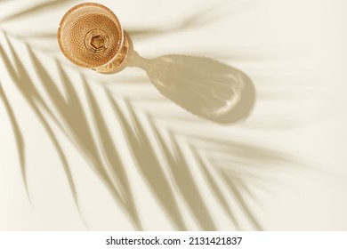 White wine glass peach color glass on beige background with palm leaf shadow, glare at sun. Minimal summer rest concept. Dry wine in colored glassware goblets style. Creative top view, pastel colors - Shutterstock ID 2131421837