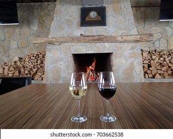 White wine and Red wine glasses on wooden table with fireplace in backdrop