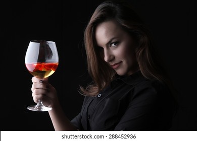 white wine and strawberries in a crystal glass - a beautiful young smiling brunette with large breasts in a black sexy dress 