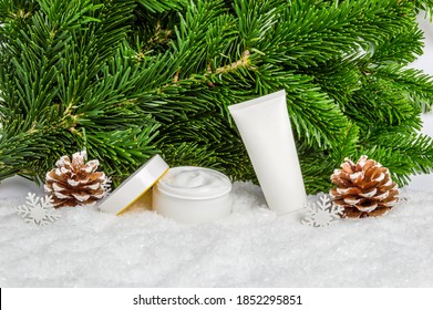 White Winter Skin Care Cosmetic Products In Snow With Christmas Tree And Pine Cones. Face Cream Jar And Hand Creme Tube. Organic Skin Moisturizer, Nourishing Mask And Body Lotion Mockup