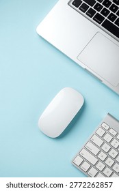 White wireless computer mouse, keyboards and laptop arranged on a light blue background in a clean minimalist modern tech setup. Top view with copy space.