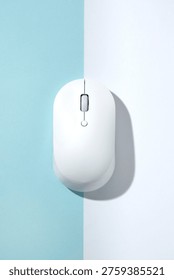 A white wireless computer mouse on a bisected light blue and white background. Top view, flat lay.