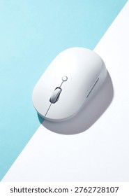 A white wireless computer mouse on a bisected light blue and white background. Top view, flat lay.