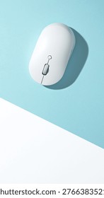 A white wireless computer mouse on a bisected light blue and white background. Top view, flat lay.