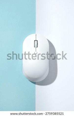 A white wireless computer mouse on a bisected light blue and white background. Top view, flat lay.