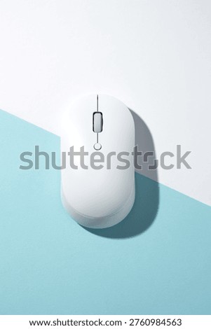 A white wireless computer mouse on a bisected light blue and white background. Top view, flat lay.