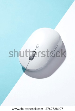 A white wireless computer mouse on a bisected light blue and white background. Top view, flat lay.