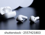 White wireless headphones pods with white charging case on dark background. Selective focus. Photo. Copy space. Close-up