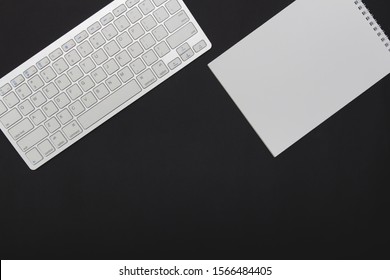 White wireless keyboard and notepad on a black background Copy space