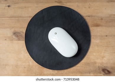 White Wireless Mouse On A Black Round Leather Mouse Pad On A Wooden Surface