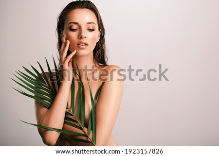 White woman with healthy skin of body and palm leaves. Tanned body of an attractive girl with green plants. Large palm leaves cover the body.