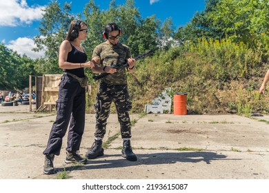 White Woman Instructing White Man How To Use Submachine Gun. Firearms Training At Shooting Range. Client With Instructor Wearing Safety Gear. Horizontal Shot. High Quality Photo