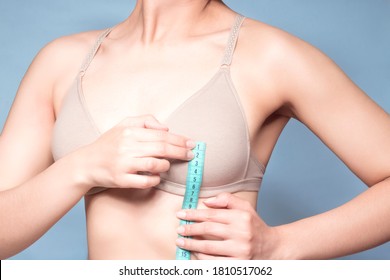 White woman with nude bra with a tape measure or measurement (Meter) measuring the middle part of the bust (Nipple) in a blue studio background