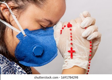 White Woman Praying Wearing Blue Mask With A Third In Her Hands, Protection Against Coronavirus. In Brazil.