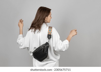 White Woman Wearing White Jeans, Shirt and Crossbody Black Leather Belt Bag over Grey Background