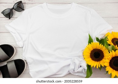 White Womens Cotton T Shirt Mockup With Sunflowers, Summer Shoes Sandals And Sunglasses On White Wooden Background. Design T Shirt Template, Print Presentation Mock Up. Top View Flat Lay.