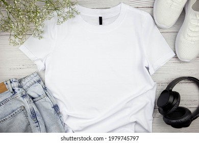 White Womens Cotton Tshirt Mockup With Flowers, Jeans, Sneakers And Black Headphones On Wooden Background. Design T Shirt Template, Print Presentation Mock Up. Top View Flat Lay. 