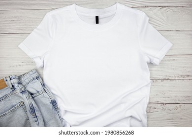 White Womens Cotton Tshirt Mockup With Blue Jeans Pants On Wooden Background. Design T Shirt Template, Print Presentation Mock Up. Top View Flat Lay. 
