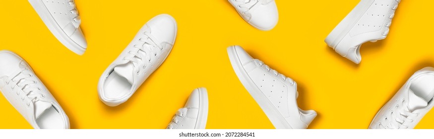 White women's leather sneakers on yellow background flat lay pattern. Stylish youth sneakers, sports shoes, genuine leather footwear. Minimalistic shoe store advertising fashion style Shoe background