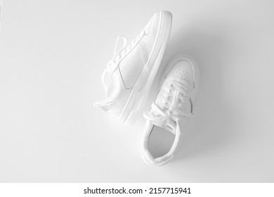 White Women's Leather Sneakers On White Background Top View Flat Lay. Stylish Youth Sneakers, Sports Shoes, Genuine Leather Footwear. Minimalistic Shoe Store Advertising Fashion Style Shoe Background