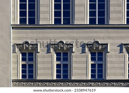 white wood windows in classic old exterior elevation with decorative trims. stucco facade closeup detail. flat frontal view. old european architecture. office space for rent. bright summer sunlight