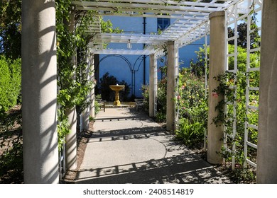 a white wooden awning in the garden covered with lush green plants and colorful flowers with stone pillars and a water fountain at the end of the walk way at Huntington Library and Botanical Garden