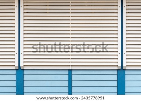 white wooden blinds on a dark window in daylight on a wooden wall made of horizontal blue boards
