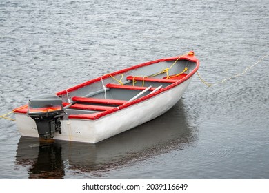 A white wooden boat, fishing boat,  with red trim and interior. The motorboat is moored with a rope. The vessel is reflected in the shallow clear water. There's a rope around the bow of the boat.