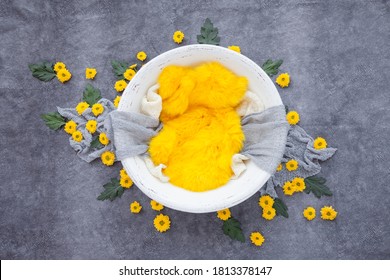 white wooden bowl for a photo shoot of a newborn baby, decorated with yellow flowers, a gray scarf and yellow fur on a dark gray background