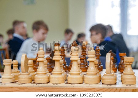 white wooden chess pieces on the board, on a blurred background of children playing chess                              