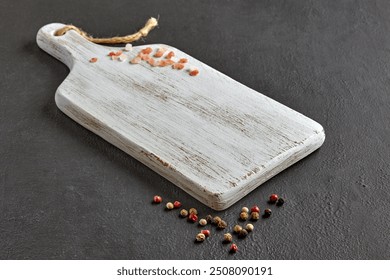 white wooden cutting board with scattered peppercorns and coarse pink salt on dark stone table. - Powered by Shutterstock