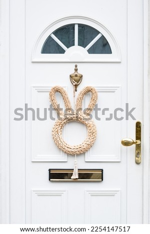 White wooden door with Easter bunny wreath. Minimalist Easter decoration